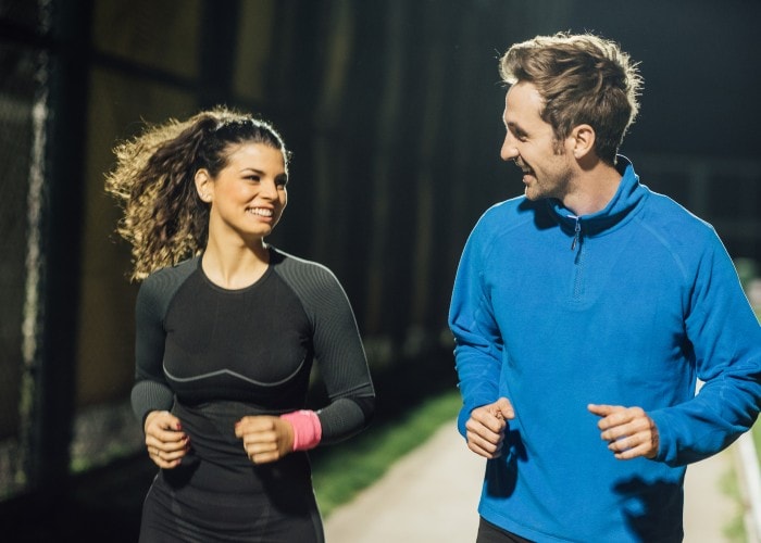 A smiling couple jogging under street lights in a park