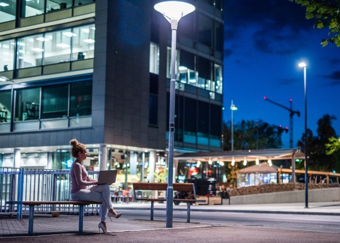 Woming working at her laptop on a bench in a city at night