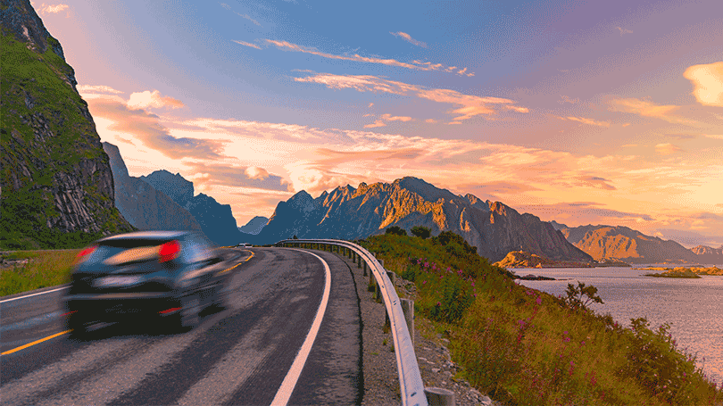 Car on scenic road by fjord in sunset