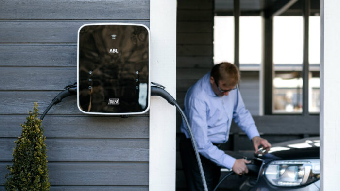 eRange® Duo charging station with two connected cables in the foreground, man connecting a charging cable to car in the background.