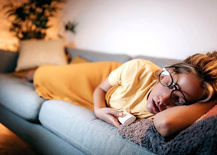 A lady is sleeping on the sofa with her glasses.