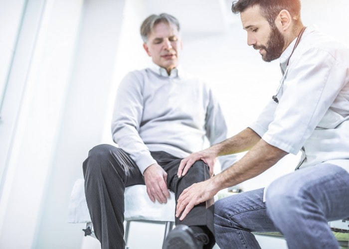 Mannlig lege kjenner på kneet til en middelaldrende mannlig pasient