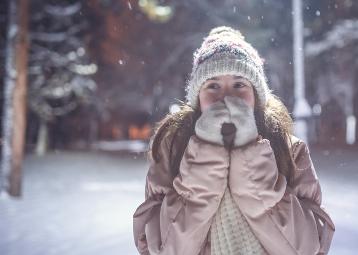 A smiling young girl warming her hands with her breath in winter under a park light