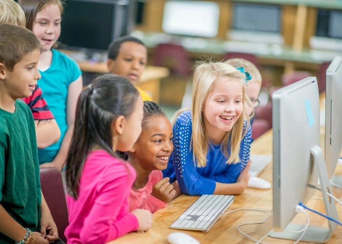 Smilende skolejenter jobber på pc