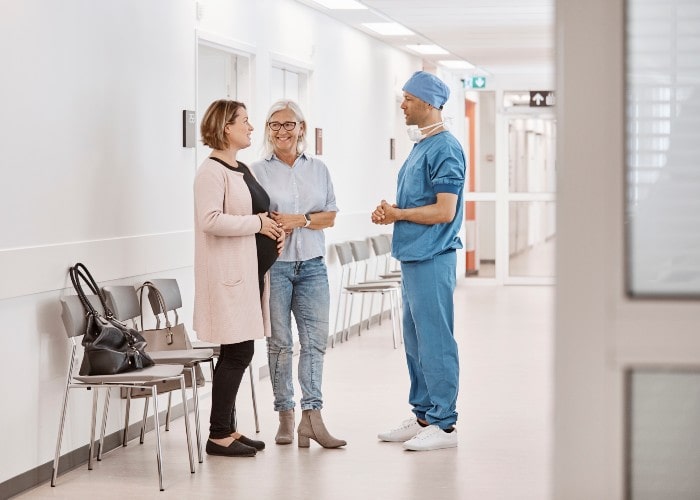 To smilende pårørende snakker med kirurg i sykehuskorridor