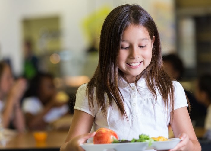 Skolejente ser på et lunsjbrett med frukt og grønsaker