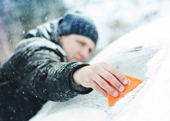 Homme en train de gratter un pare-brise glacé de voiture en hiver.